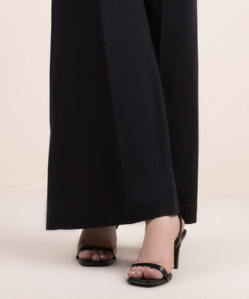 A close-up of black flowy trousers paired with high heels, focusing on the trousers and feet.