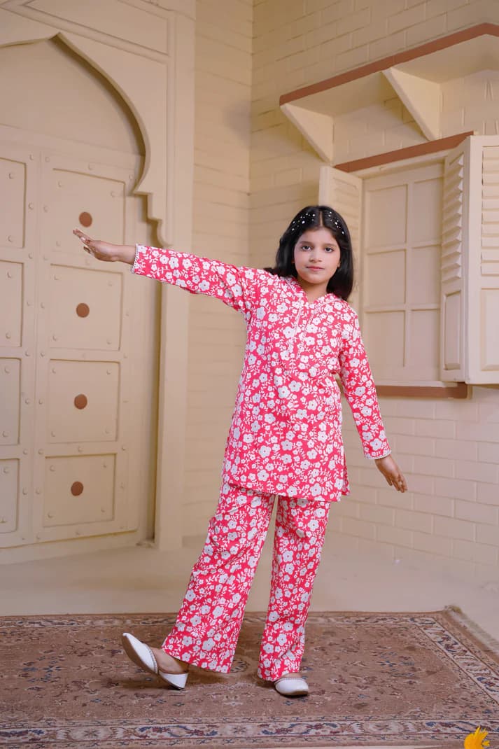 Young girl in a pink floral outfit standing in a room with wooden paneling.