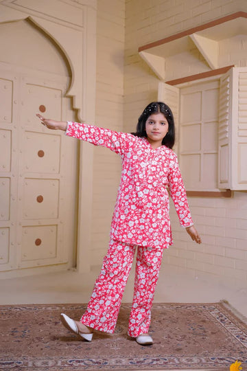 Young girl in a pink floral outfit standing in a room with wooden paneling.