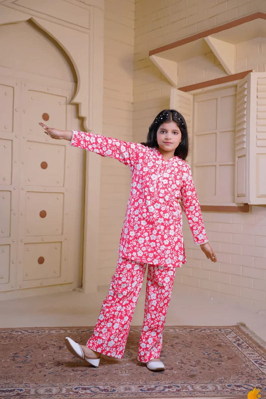 Young girl in a pink floral outfit standing in a room with wooden paneling.