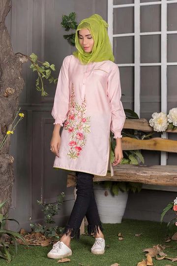 Woman wearing a light pink embroidered blouse with black pants in an outdoor setting.