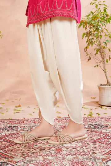 Person wearing white pants and a pink top on a patterned rug with a plant in the background