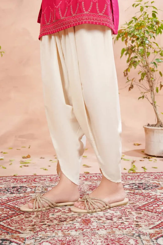 Person wearing white pants and a pink top on a patterned rug with a plant in the background