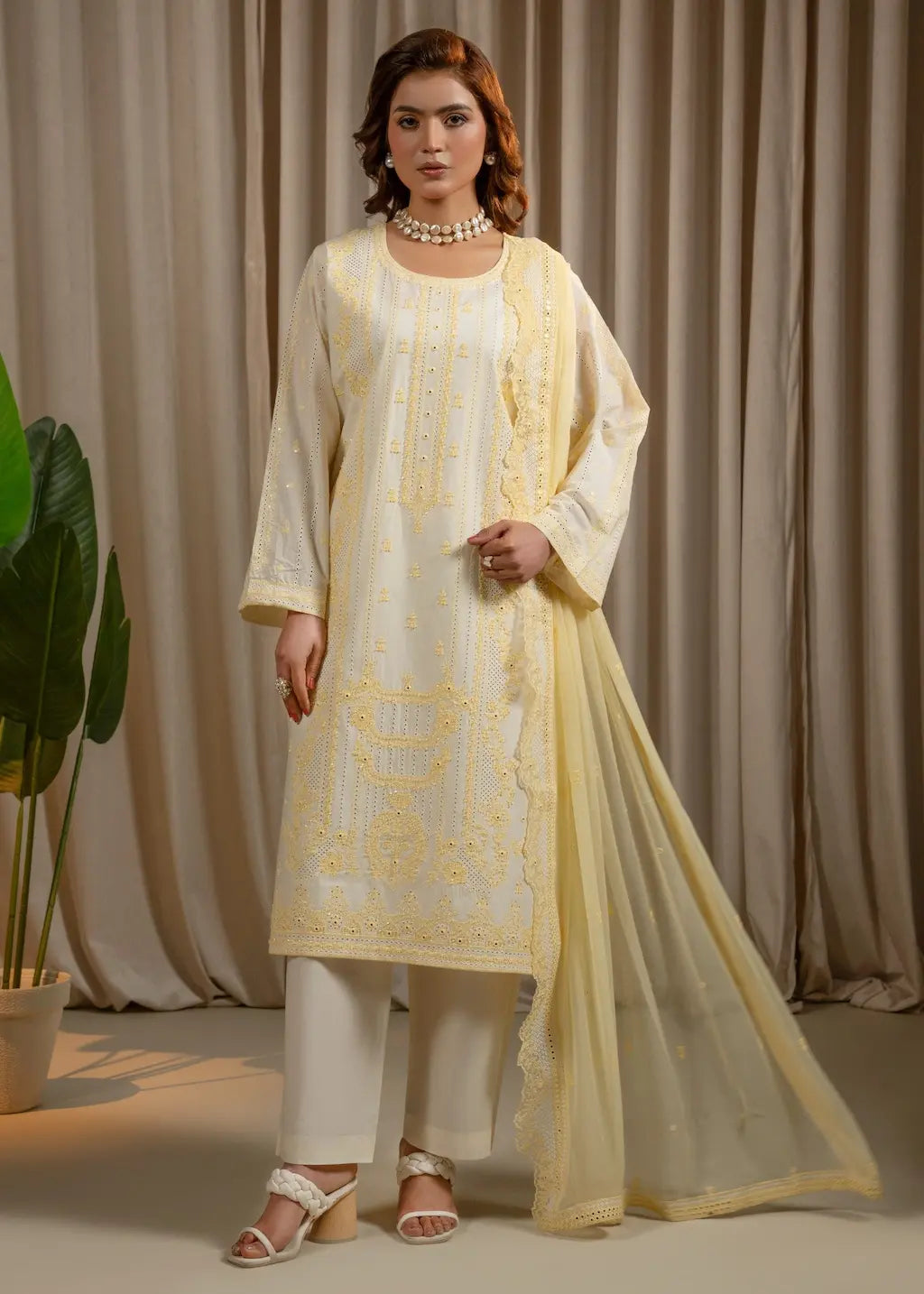 Woman wearing a light yellow embroidered outfit with a beige curtain background