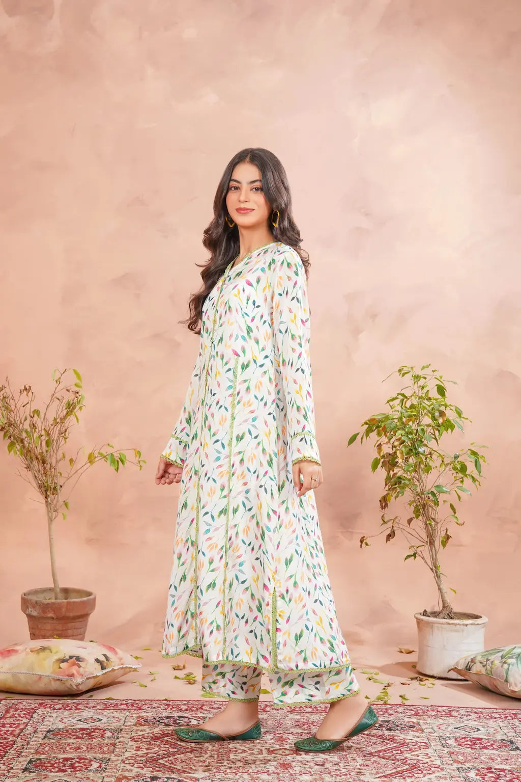 Woman in a floral dress standing in front of a pink wall with plants and pillows.