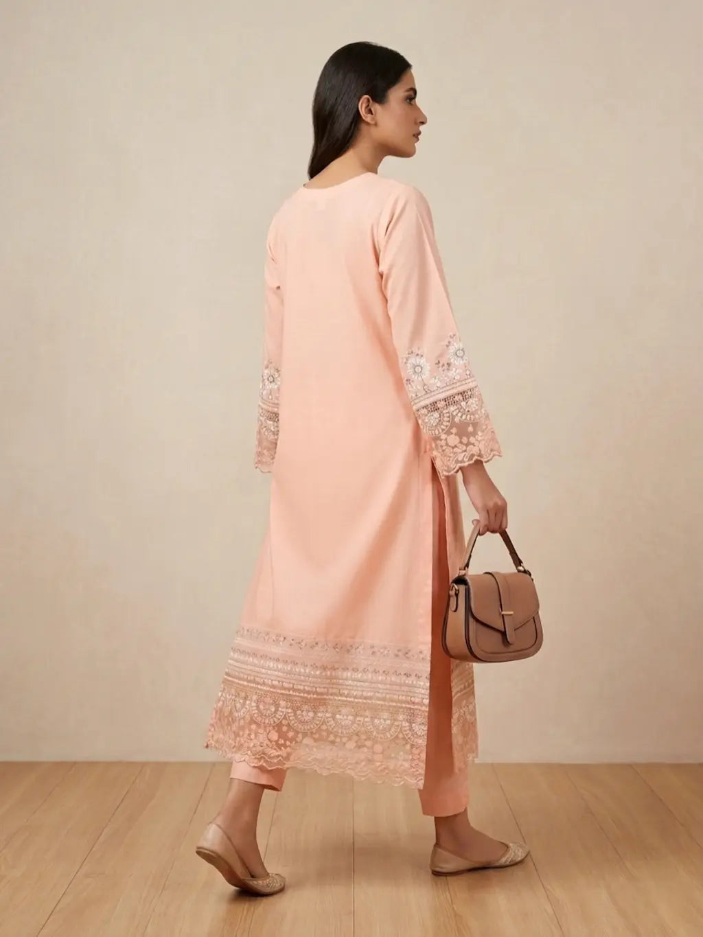Woman wearing a peach kurta with lace details and holding a brown handbag against a beige background