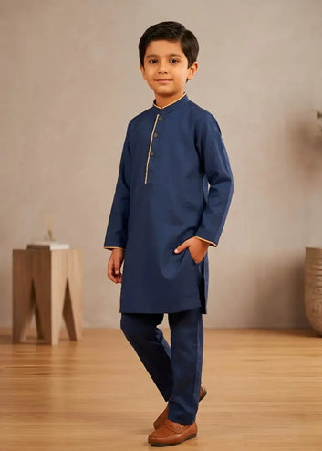 Young boy wearing a blue kurta with brown shoes standing indoors.