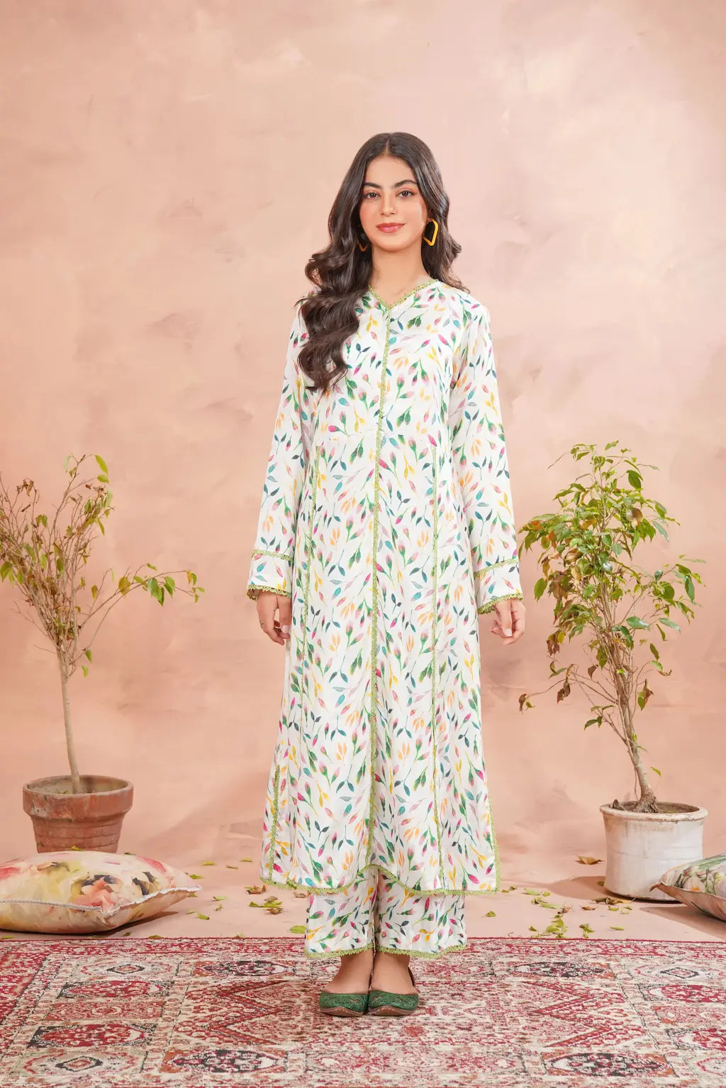 Woman wearing a floral dress standing in front of a pink wall with plants.