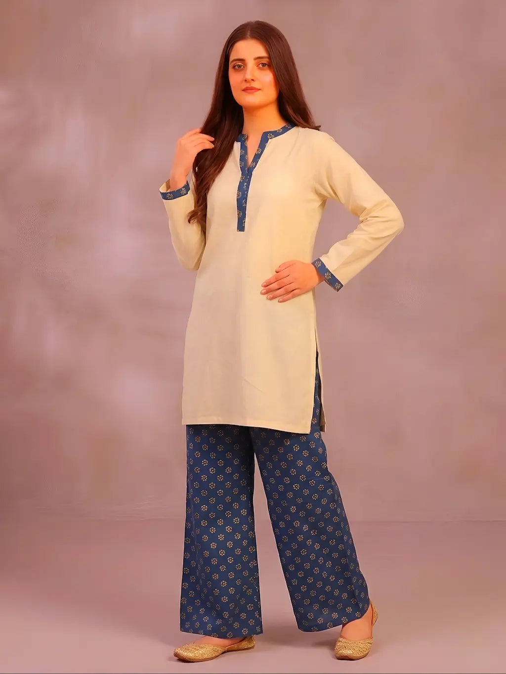 Woman wearing a cream kurta with teel patterns against a plain background
