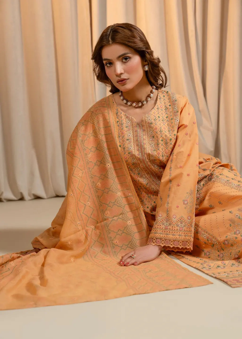 Woman in an orange traditional outfit with intricate patterns sitting on a light-colored floor.