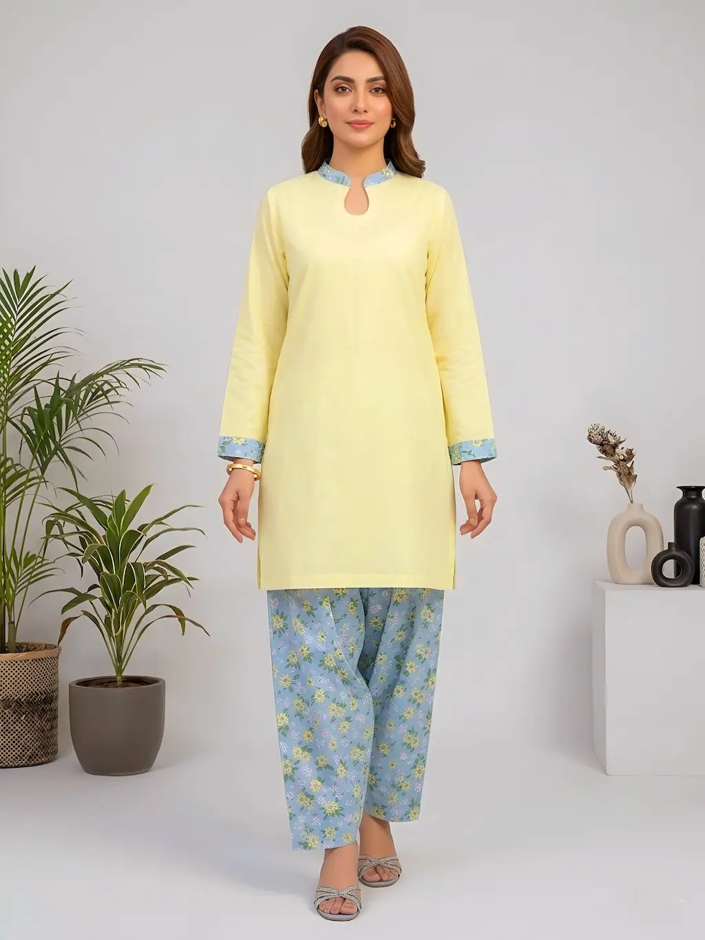 Woman wearing a light yellow kurta with blue floral shalwar on a white background