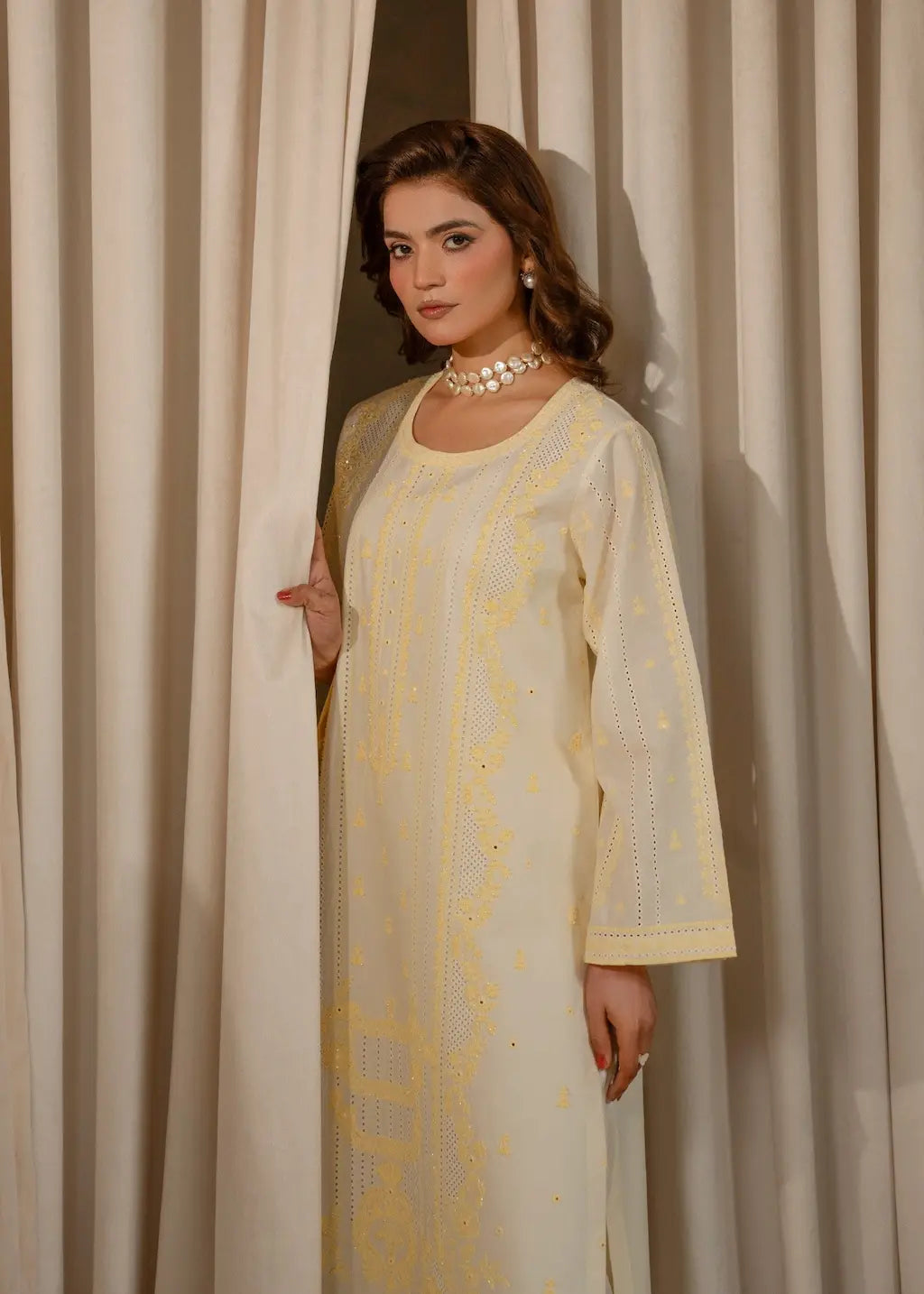 Woman wearing a light yellow embroidered kurta with a plain background