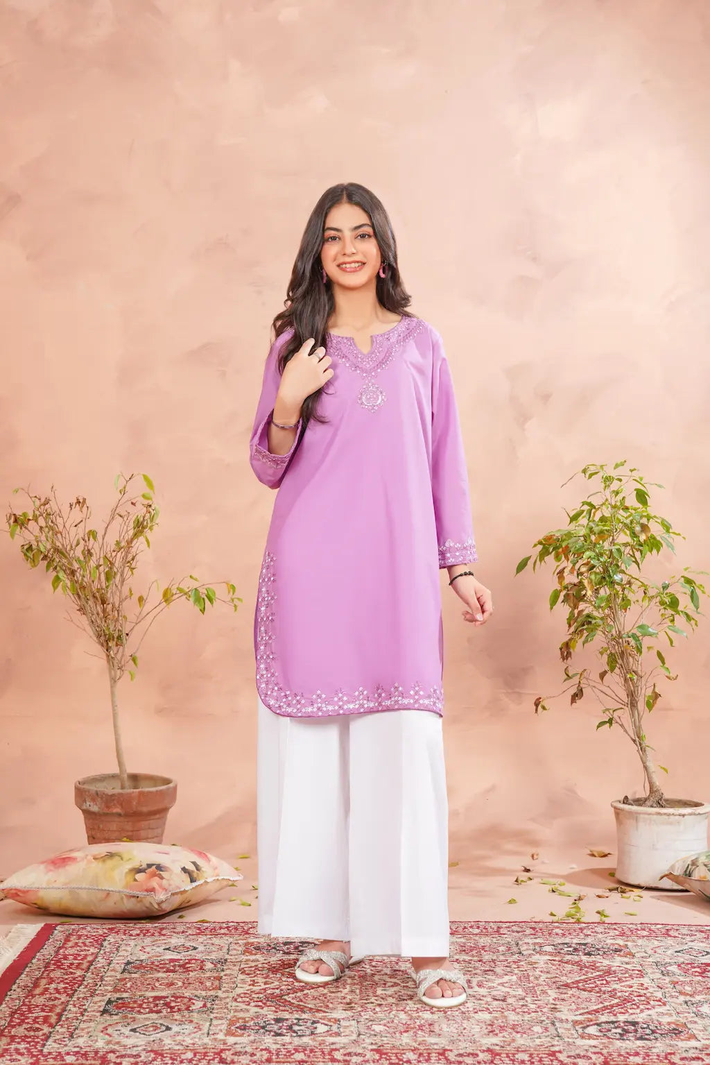 Woman wearing a purple kurta with white pants in a decorated room.