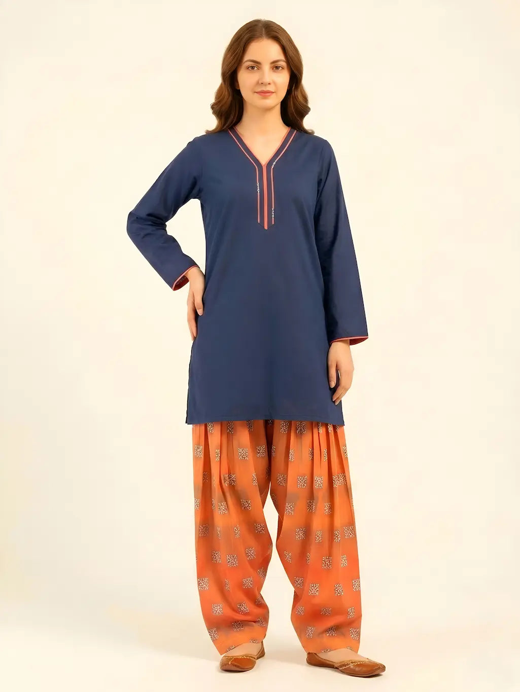 Front view of a model wearing a navy blue lawn short-length shirt with coral piping on the V-neck, paired with a digital printed rust-orange Farshi shalwar and brown leather khussas.