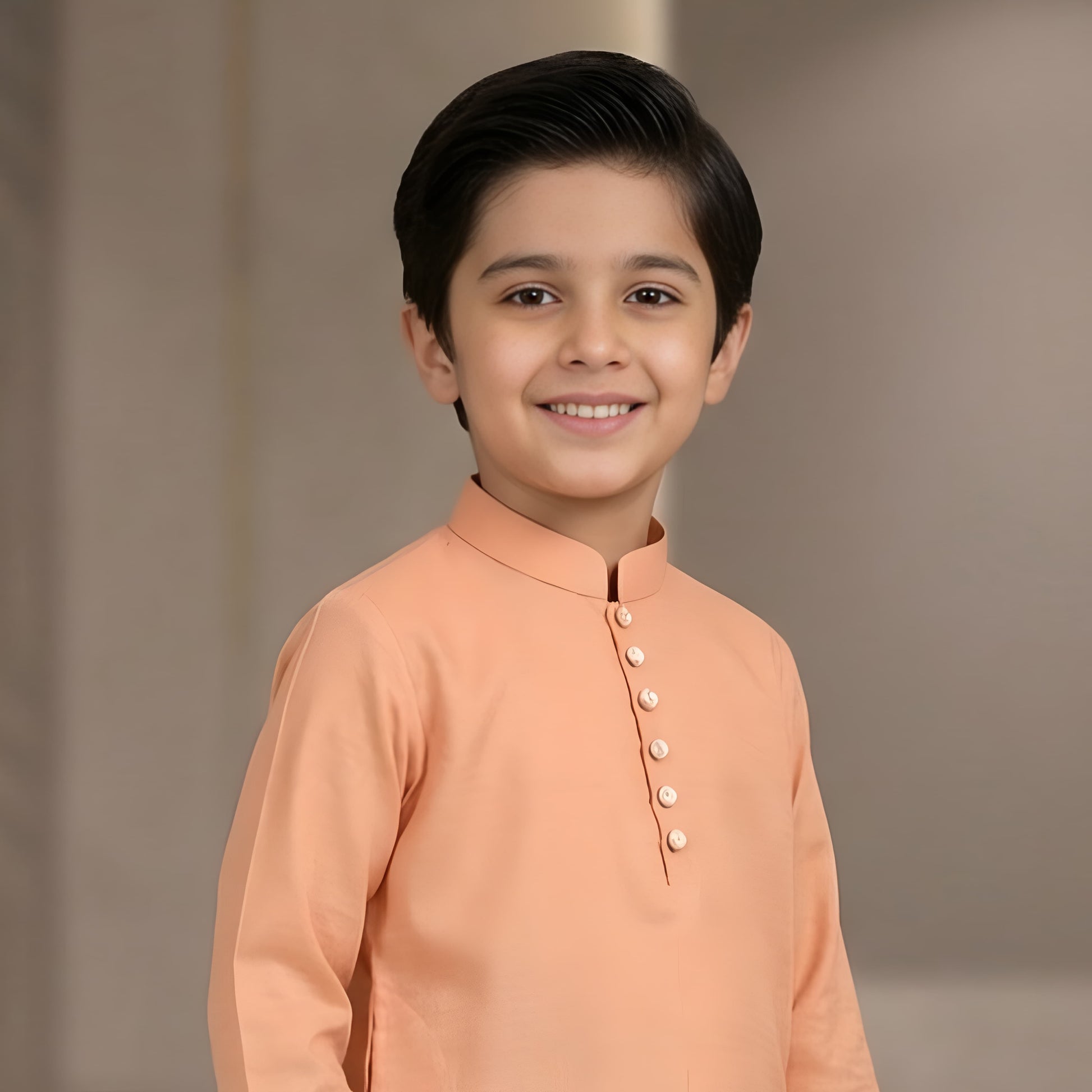 Young boy wearing a peach kurta against a plain background