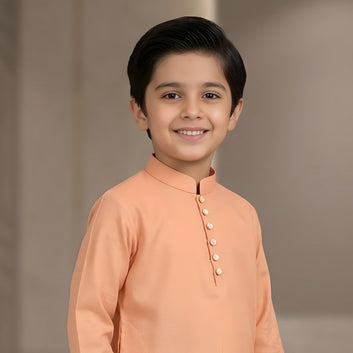 Young boy wearing a peach kurta against a plain background