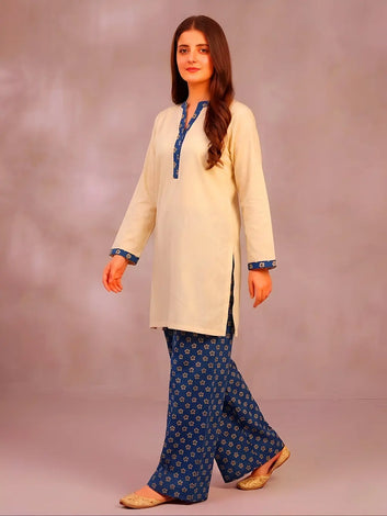 Woman wearing a cream kurta with teel trousers against a plain background