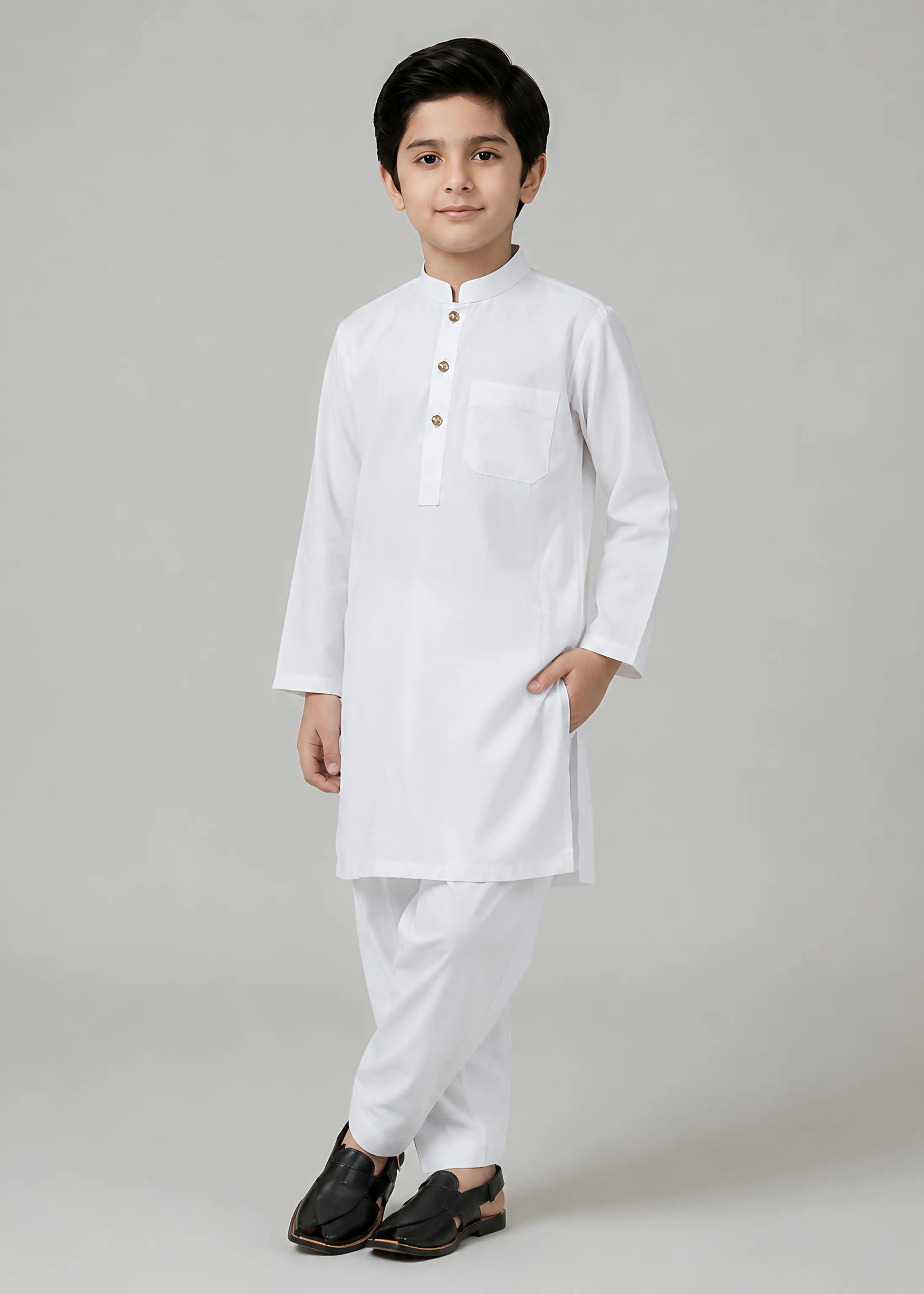 Young boy wearing a white kurta with black shoes on a light gray background