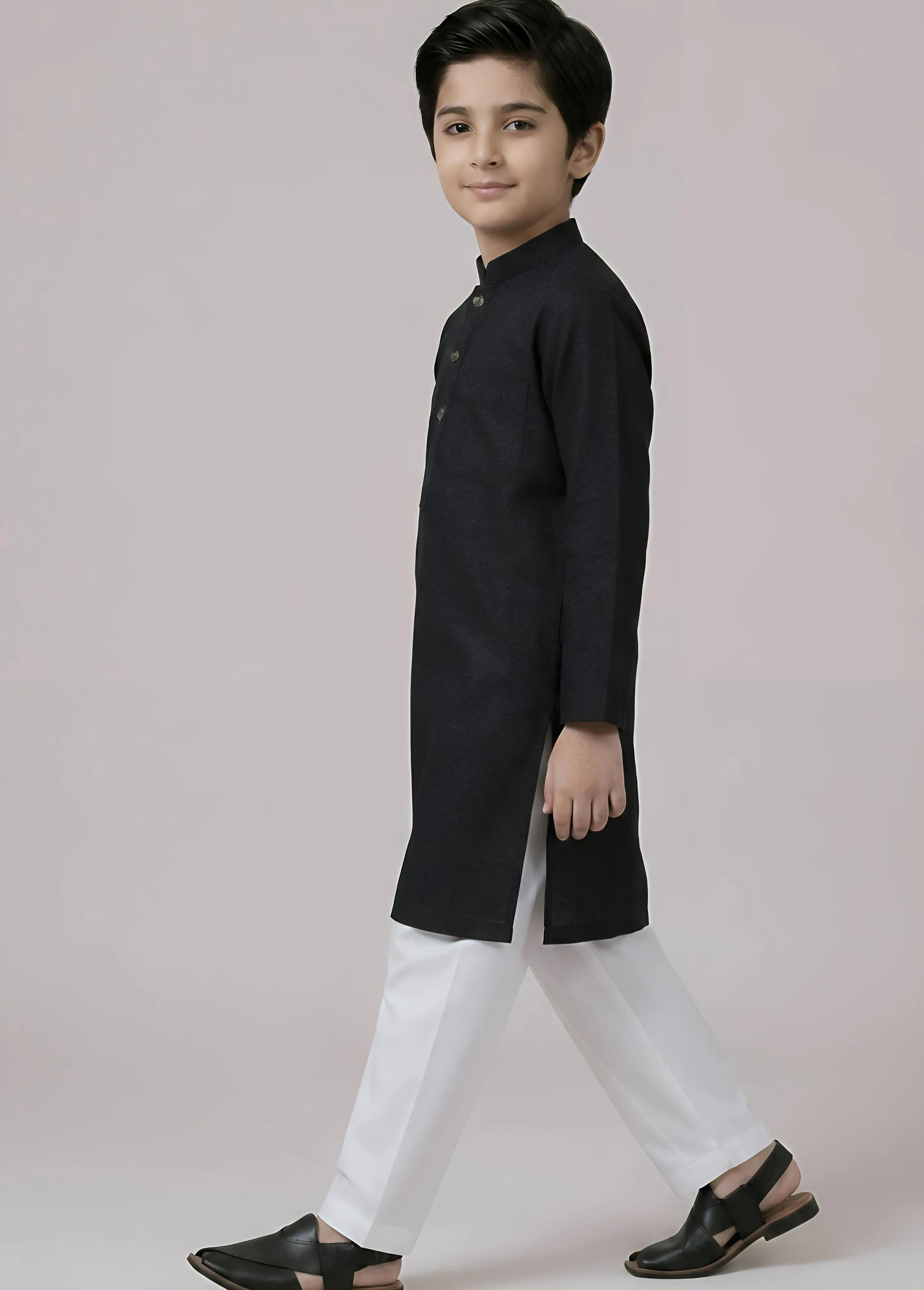 Young boy wearing a black kurta with white pants on a plain background