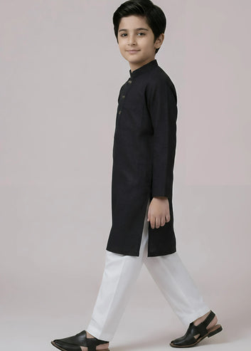 Young boy wearing a black kurta with white pants on a plain background