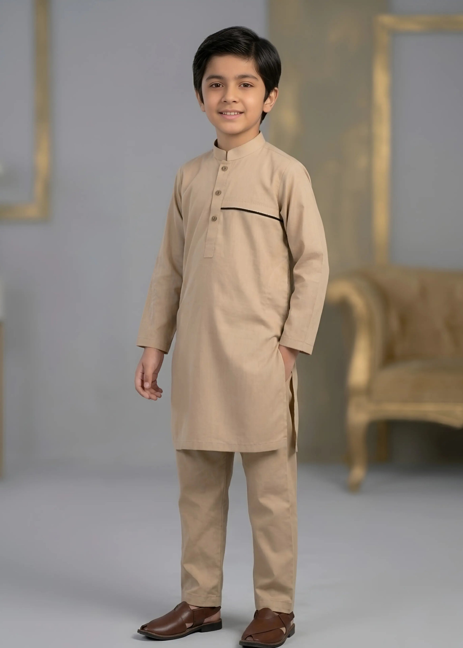 Young boy wearing a beige kurta with brown shoes in a studio setting