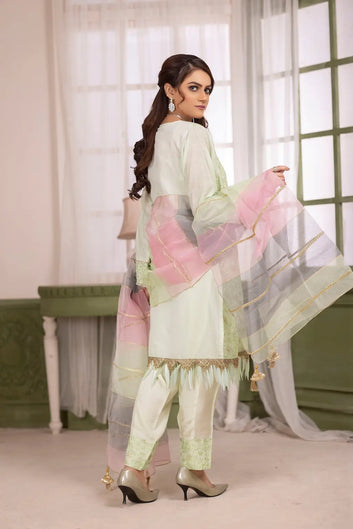 Woman in a light green traditional outfit with pink dupatta standing indoors.