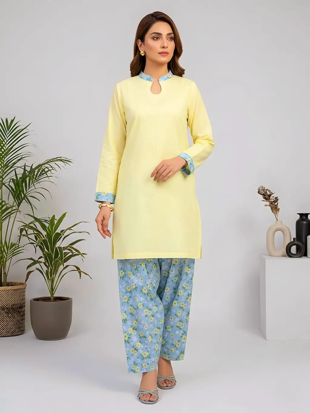 Woman wearing a light yellow kurta with blue floral shalwar in a minimalistic setting.