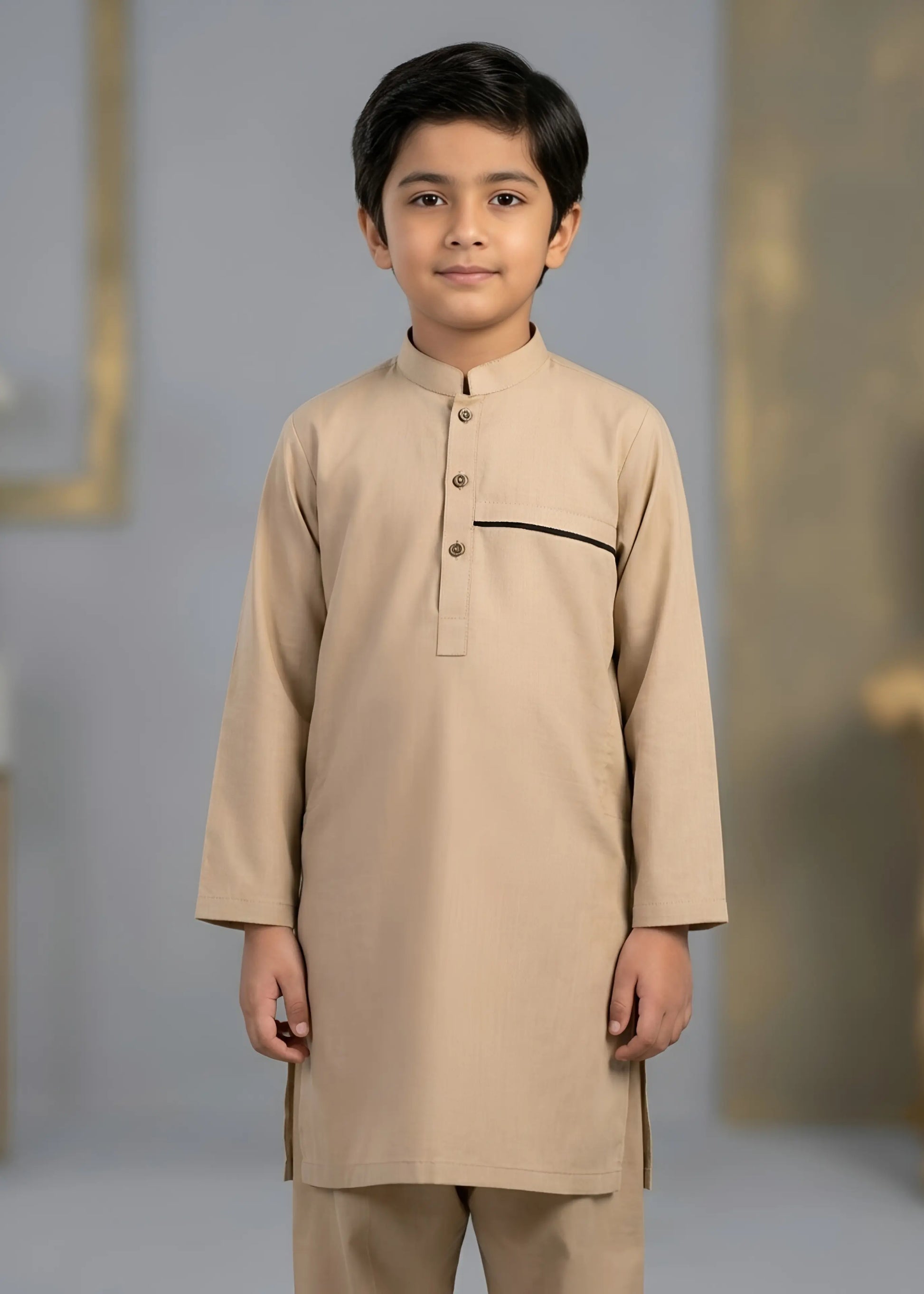 Young boy wearing a beige traditional outfit against a neutral background