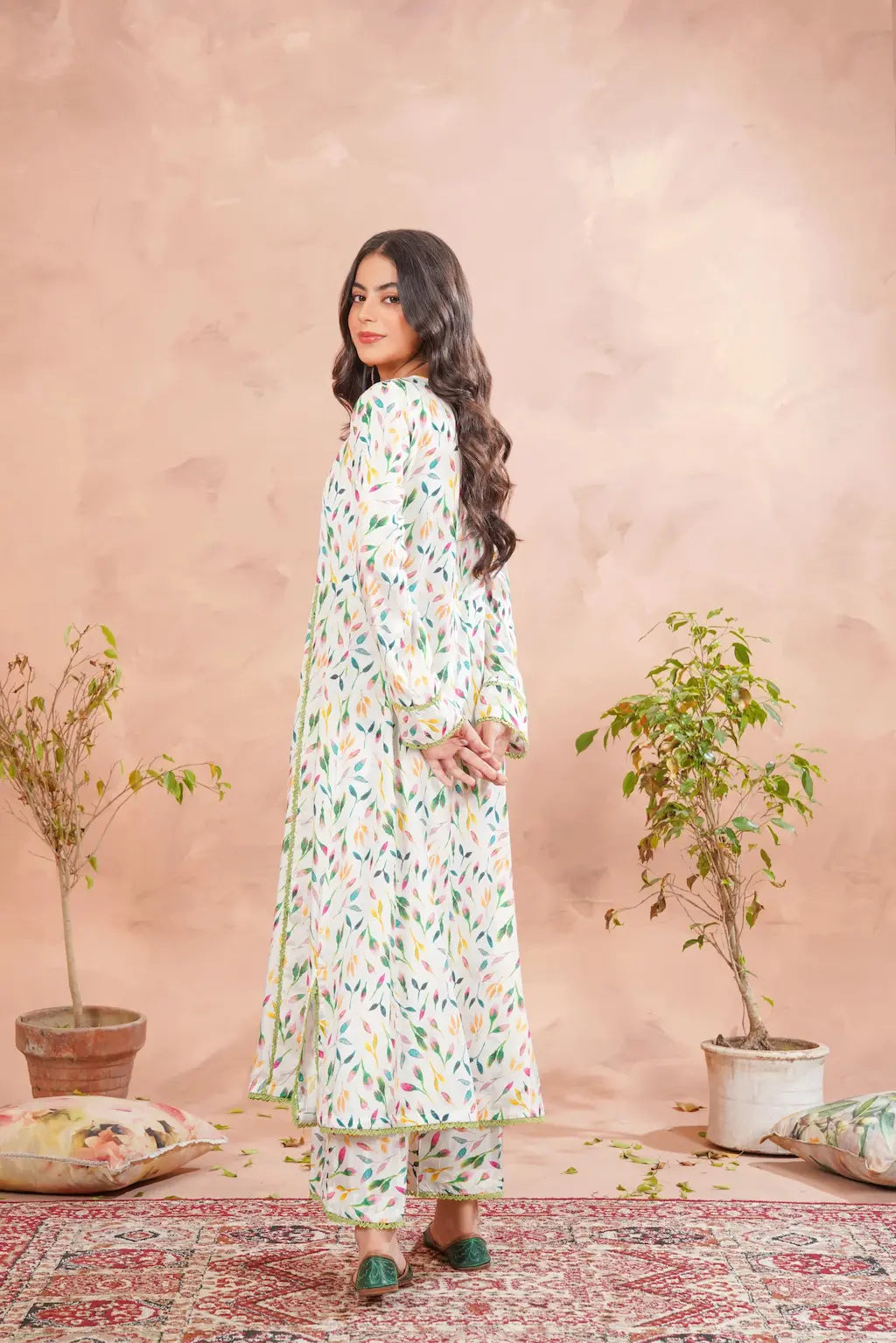 Woman in a floral dress standing in a room with pink walls and decorative plants.