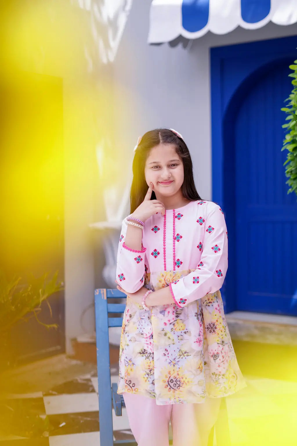 Young girl in a colorful dress standing in front of a blue door with yellow walls.