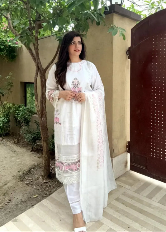 Woman in a white traditional outfit standing outdoors near a gate.