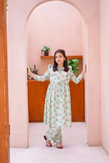 Young girl in a floral dress standing in a room with pink walls and wooden shelves.