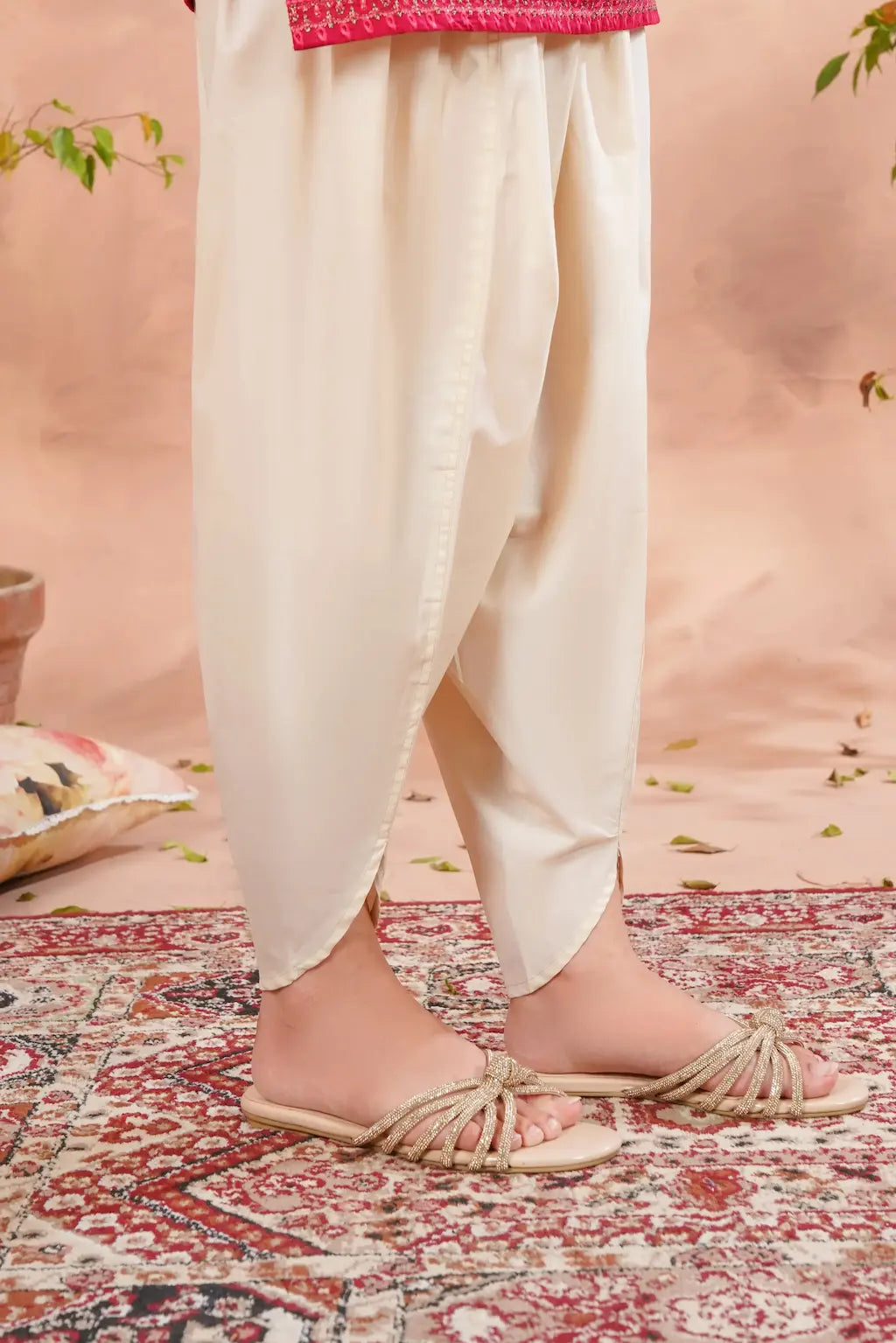 White dhoti pants worn by a person on a patterned rug with a pink background