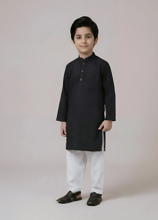 Young boy wearing a black kurta with white pants on a plain background
