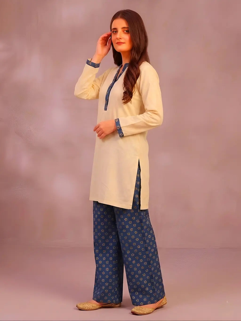 Woman wearing a cream kurta with teel patterns and matching pants against a plain background