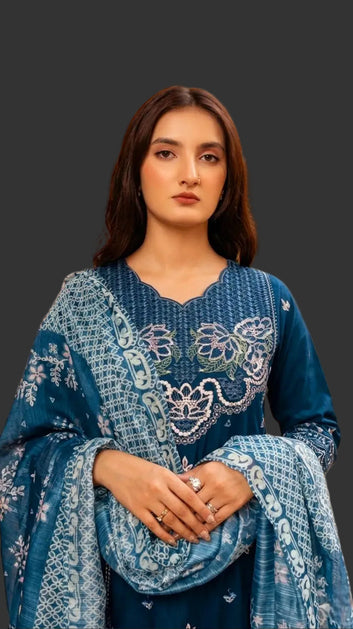 Woman in a teal blue embroidered traditional outfit standing in front of a decorative wall.