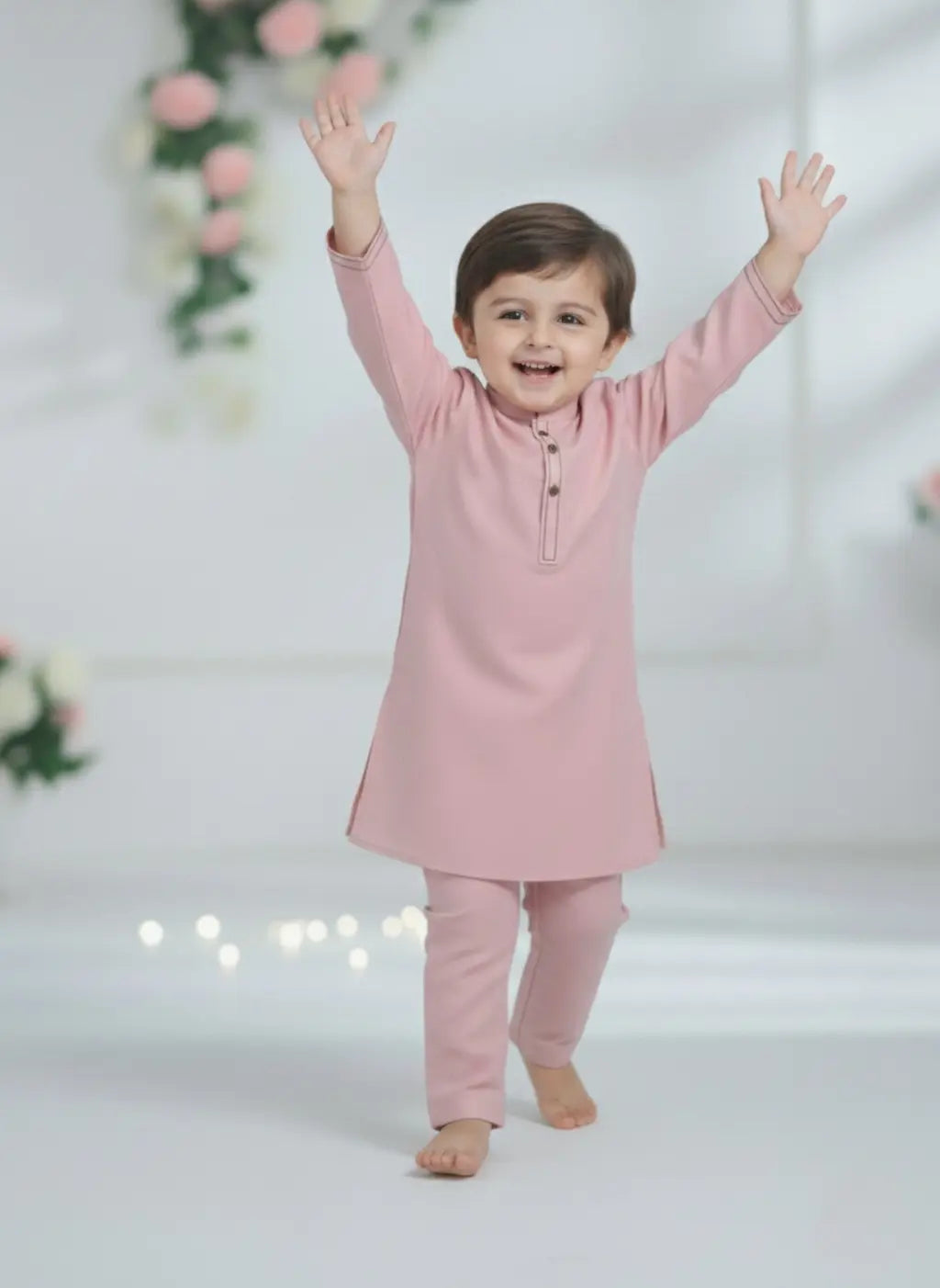 Child wearing a pink traditional outfit with arms raised against a light background