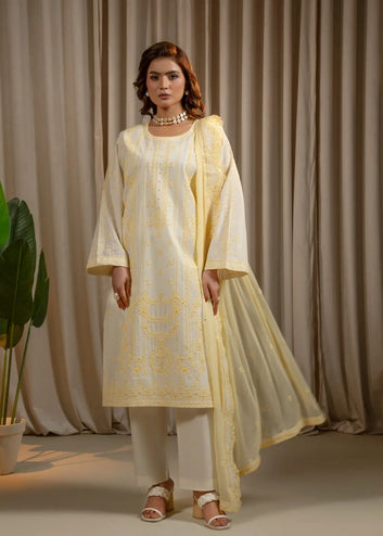 Woman wearing a light yellow and white traditional outfit with a matching dupatta against a beige curtain background.