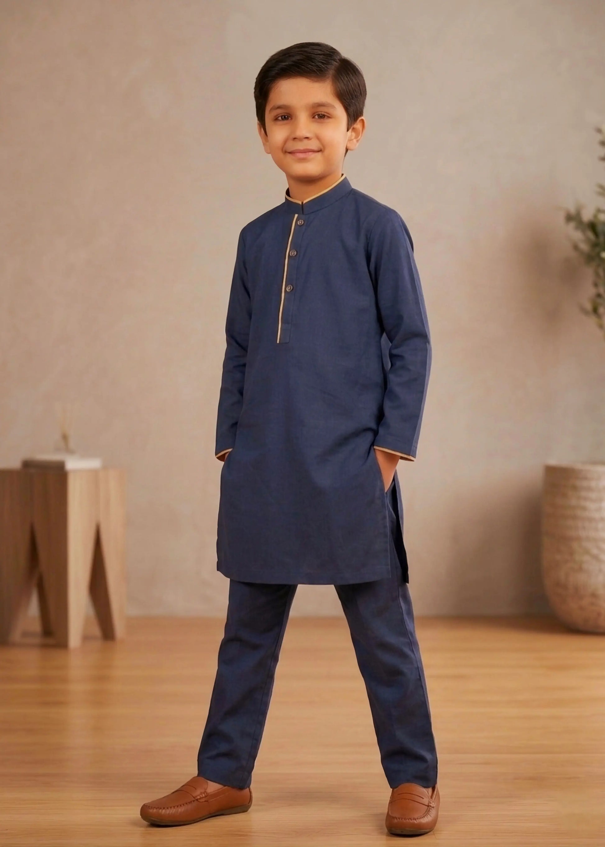 Young boy wearing a navy kurta with gold accents standing against a neutral background