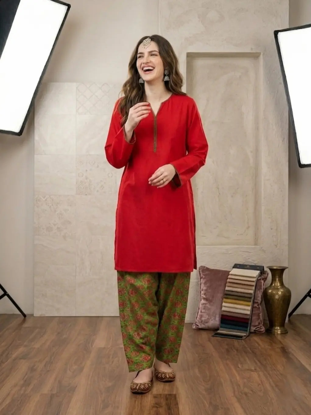 Woman wearing a red top and green printed shalwar in a studio setting.