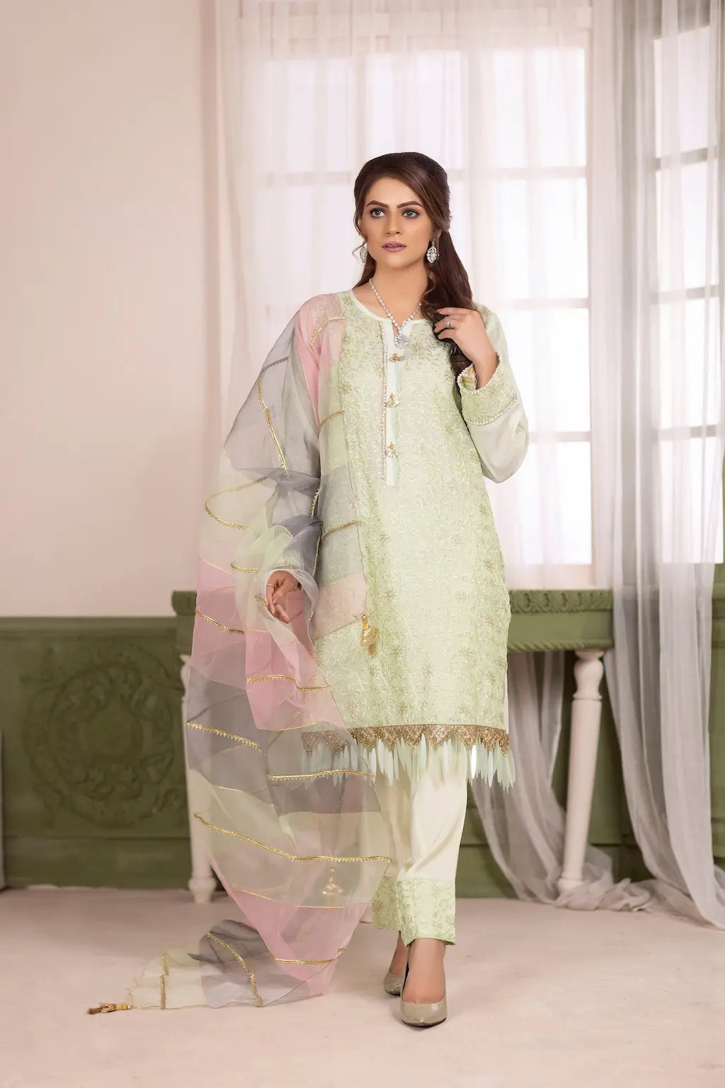 Woman wearing a light green traditional outfit with a sheer dupatta in a decorated room.