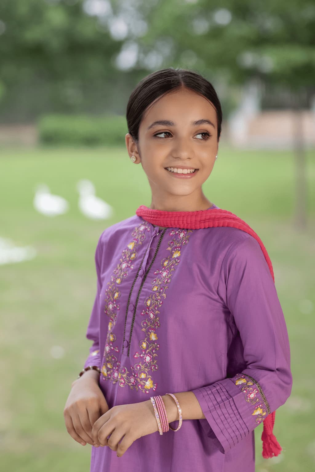 Young girl wearing a purple embroidered top with a pink shawl in an outdoor setting.