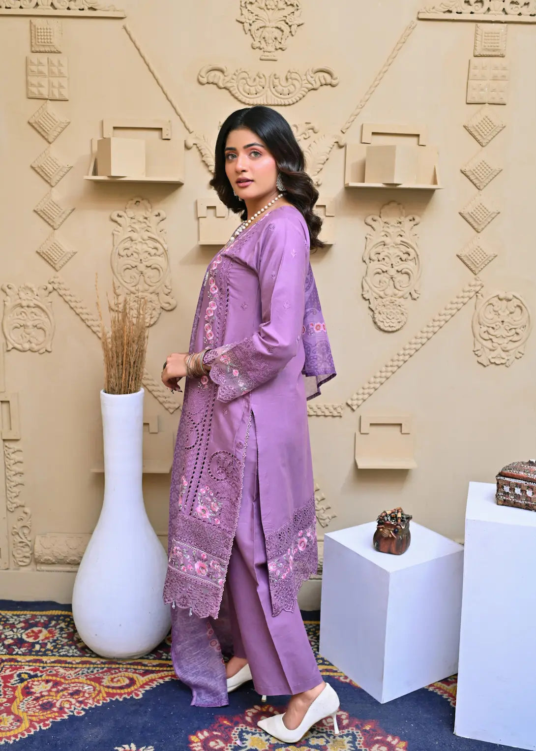 Woman in a purple traditional outfit standing against an ornate wall.