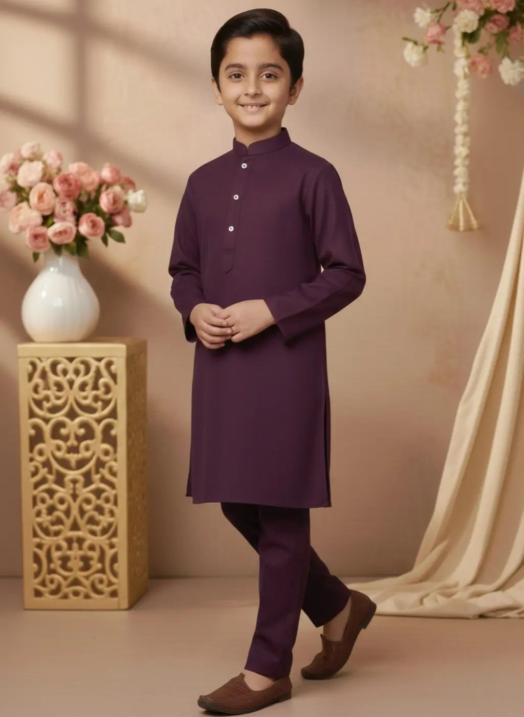 Young boy in a purple kurta standing in a decorated room with flowers and a vase.
