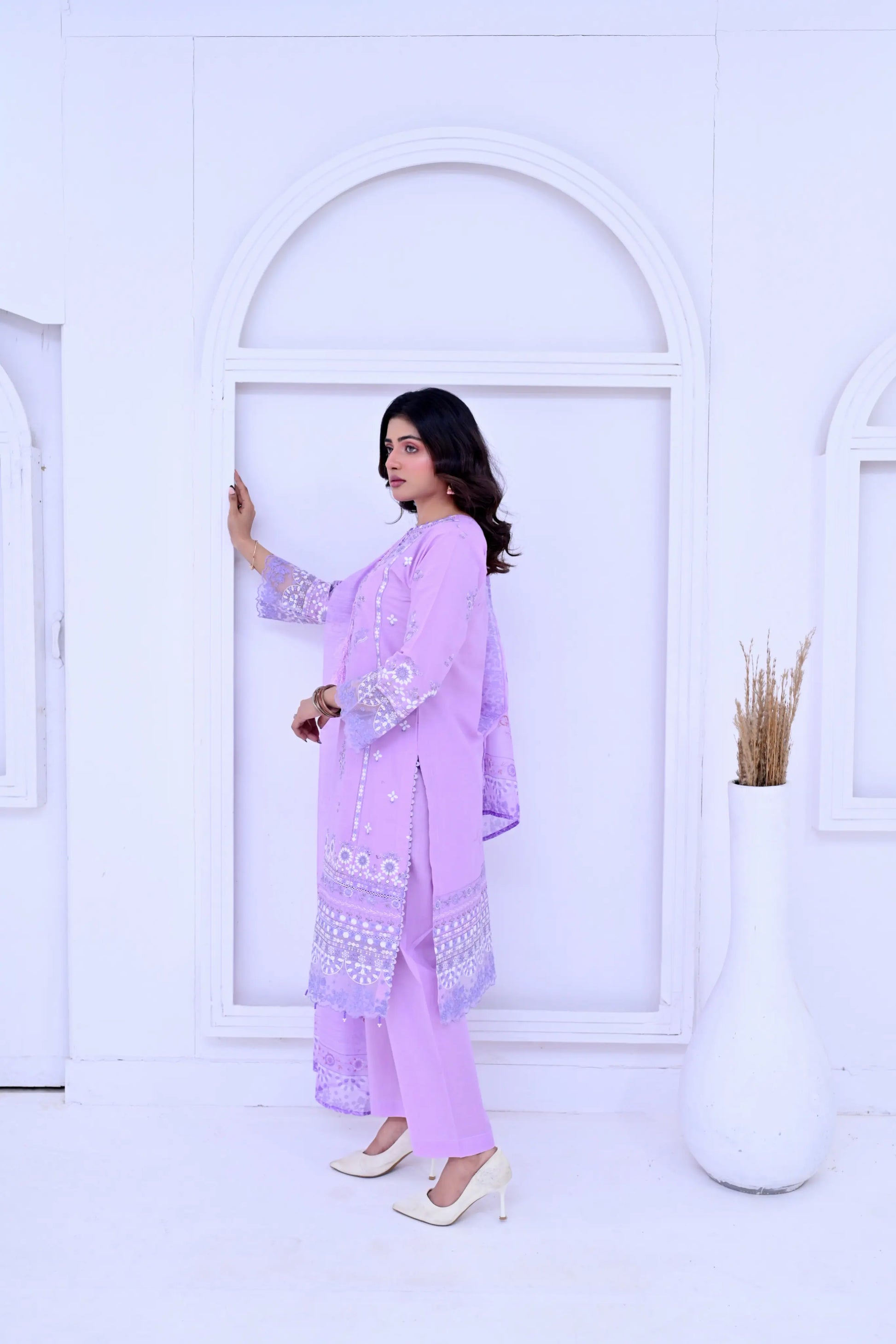 Woman in a light purple traditional outfit standing in front of a white archway.