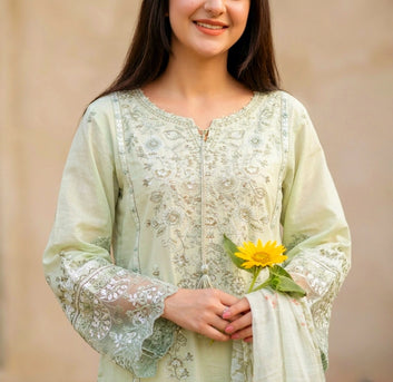 Woman wearing a light green embroidered traditional outfit holding a yellow flower against a beige background