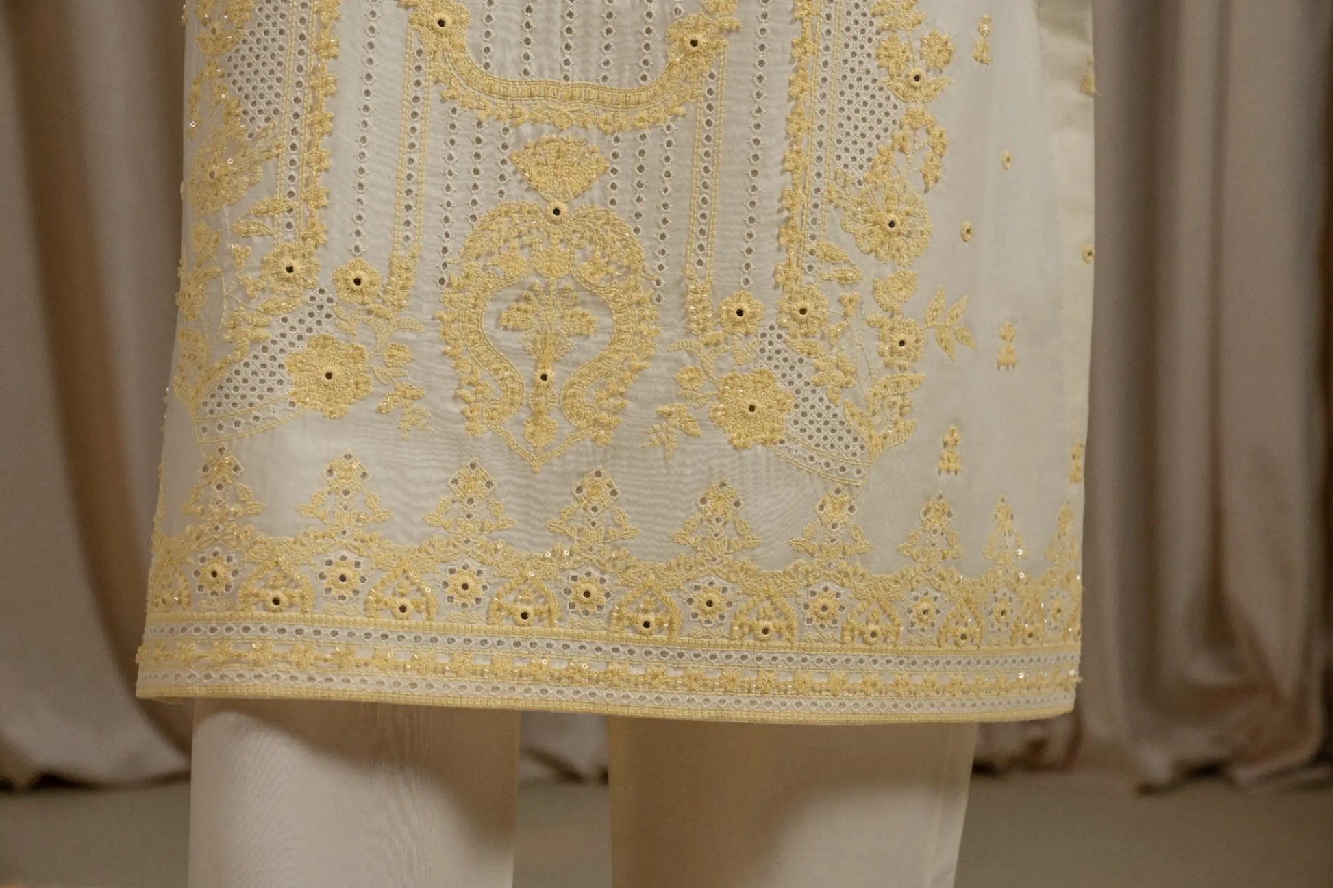 Close-up of a white fabric with yellow intricate embroidery on a neutral background