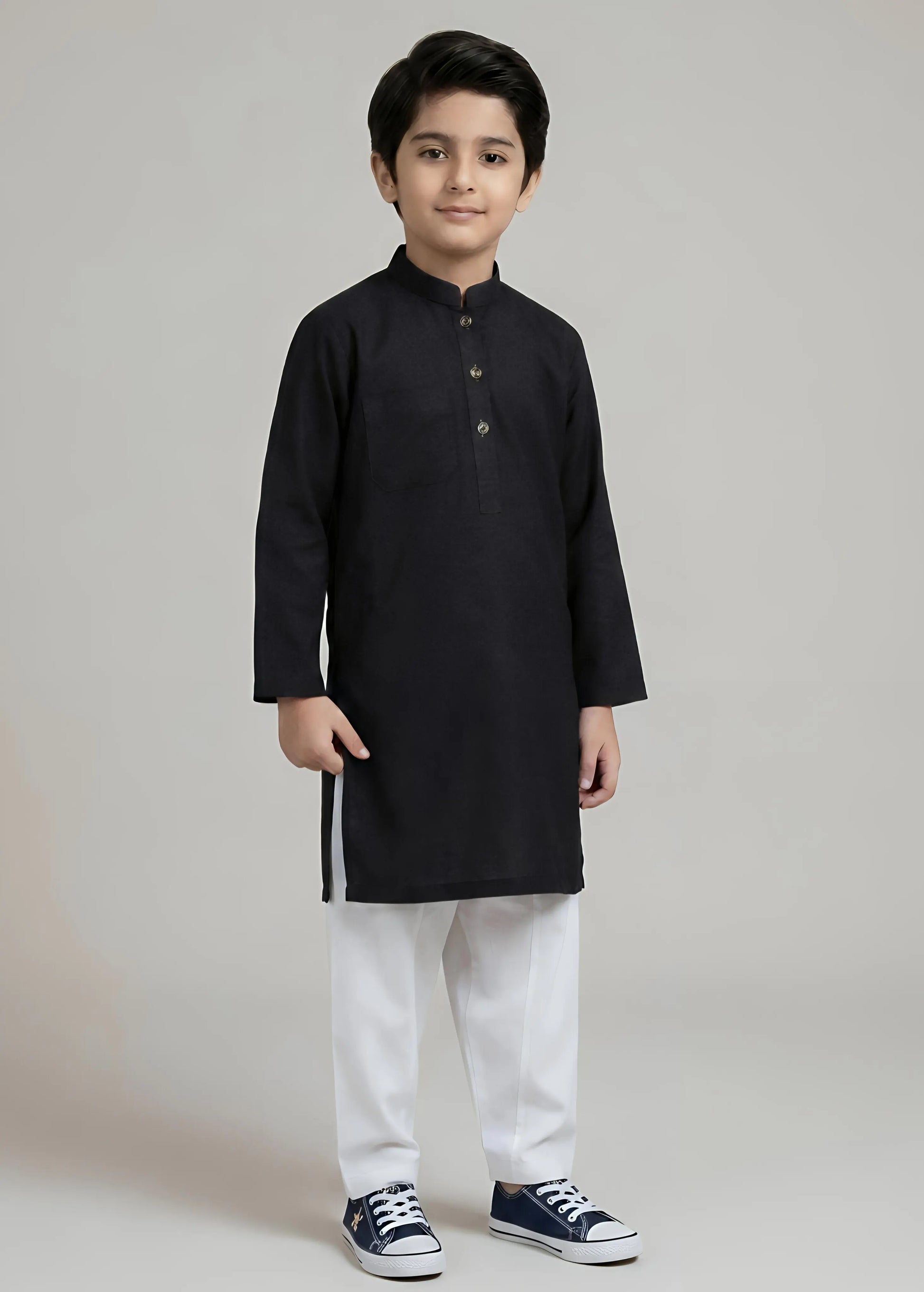 Young boy wearing a black kurta with white pants on a gray background