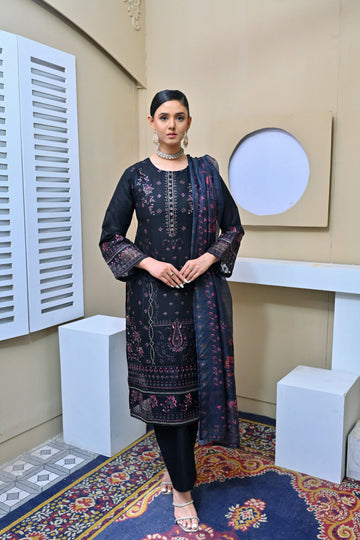 Model in a black three-piece embroidered suit with pink floral details, lace-trimmed sleeves, and a printed dupatta, posing in a minimalist studio setting.