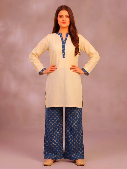 Woman wearing a cream kurta with teel printed trousers against a plain background